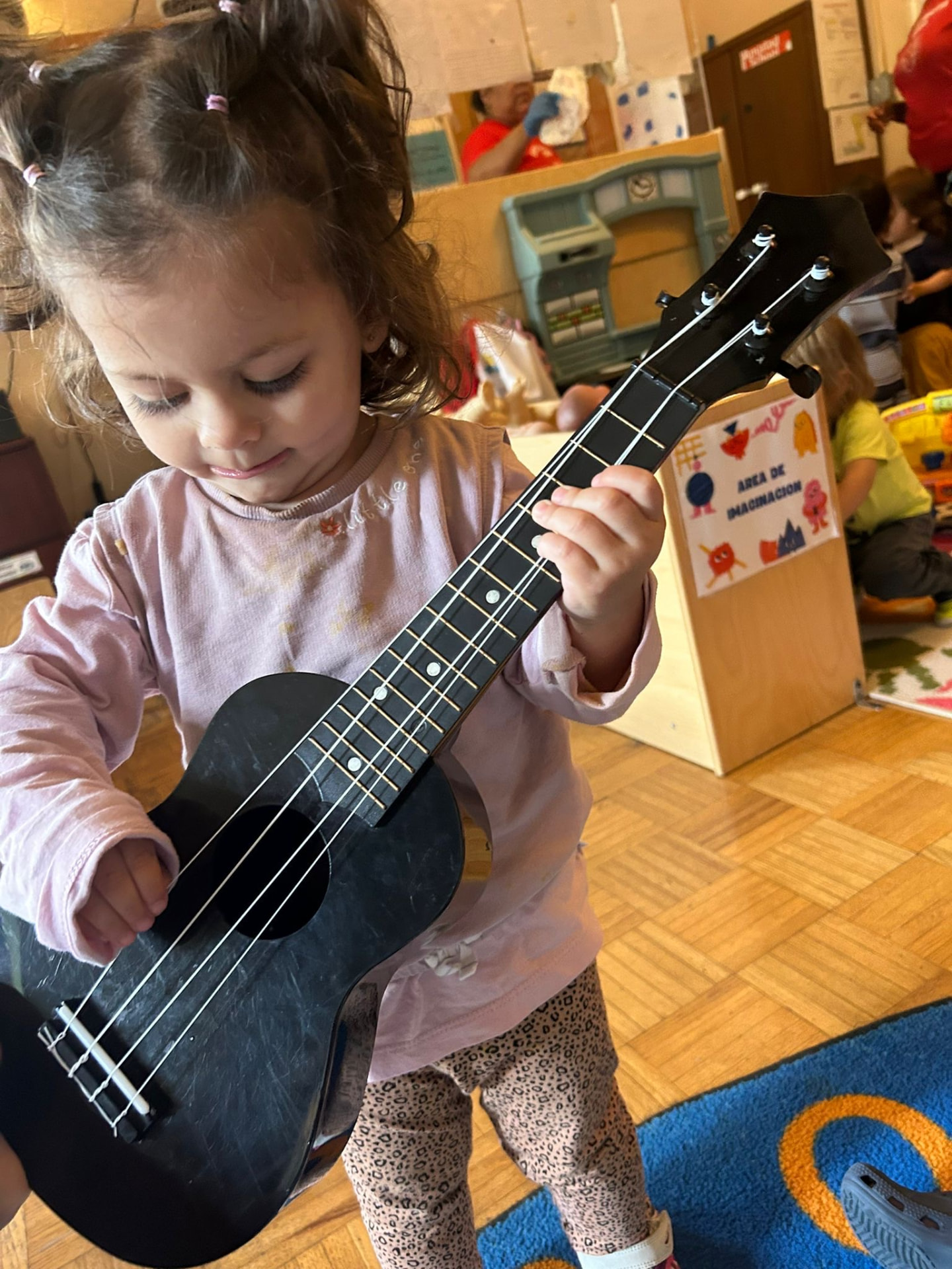 A toddler strumming a ukulele in the Little Learners classroom