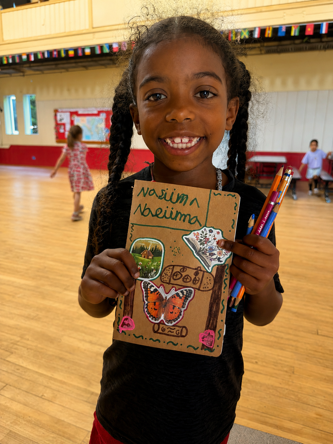 A smiling student holding up her hand-decorated notebook and colored pencils