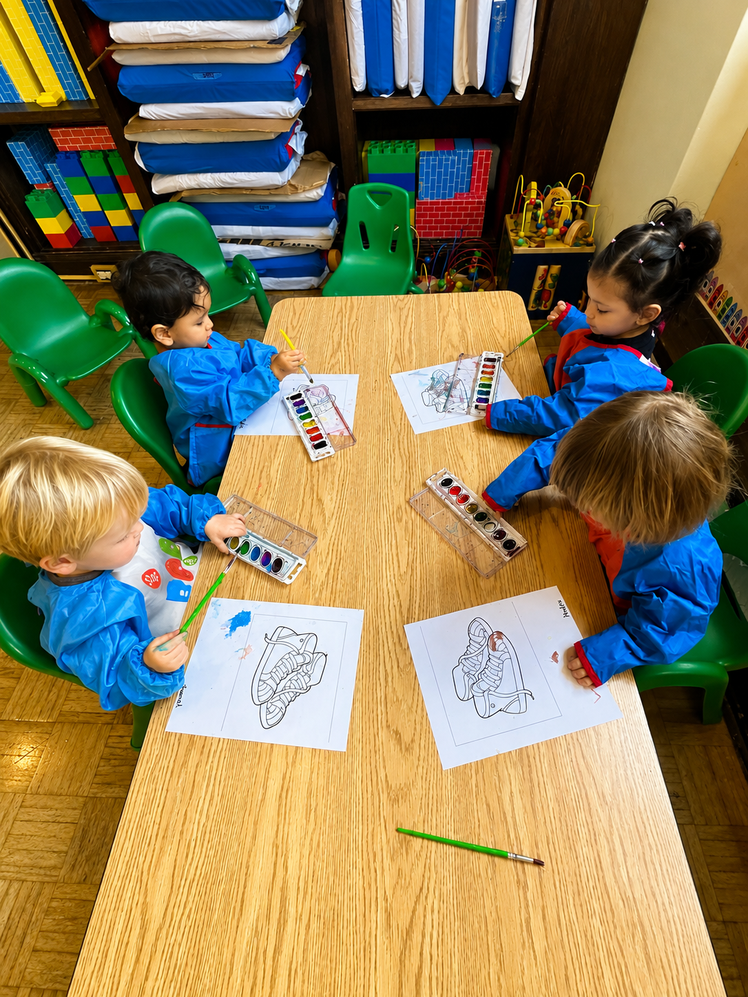 Young Little Learners painting with watercolors around a classroom table