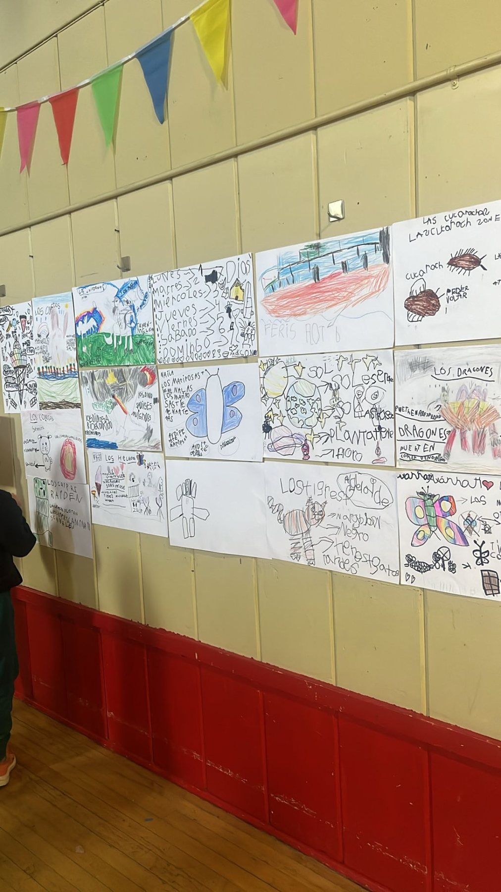 A wall of student writing and drawings in Spanish displayed in the school gym