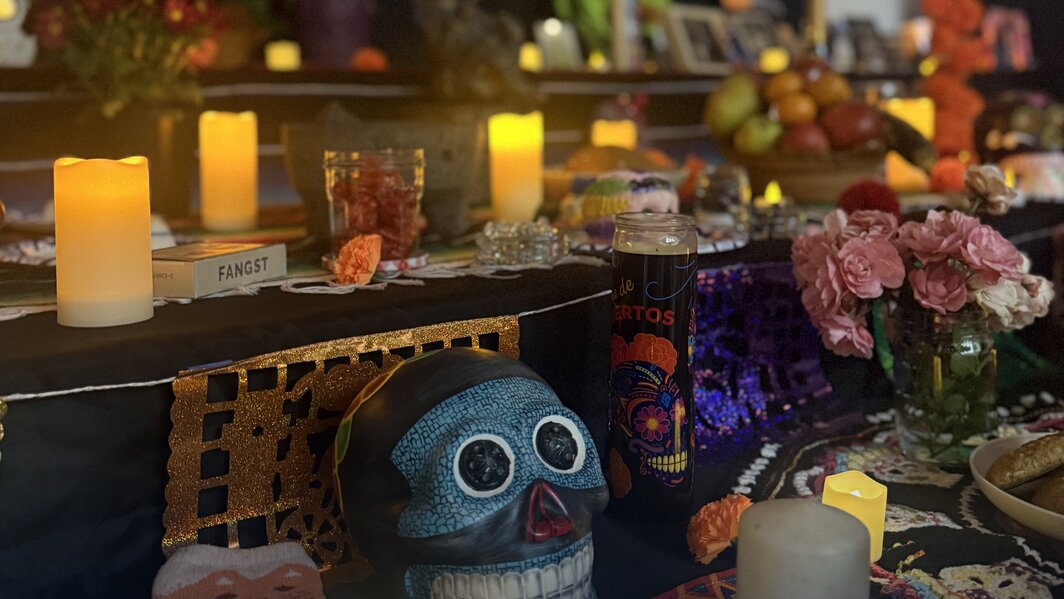 A community ofrenda at Seattle Amistad School with candles, a blue calavera, marigolds, papel picado and pink flowers.