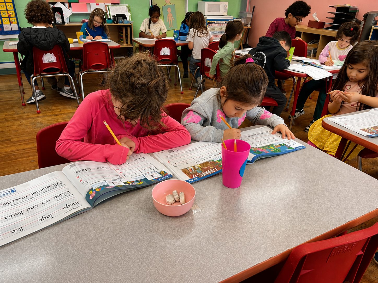 Students practicing early reading and writing at a classroom table