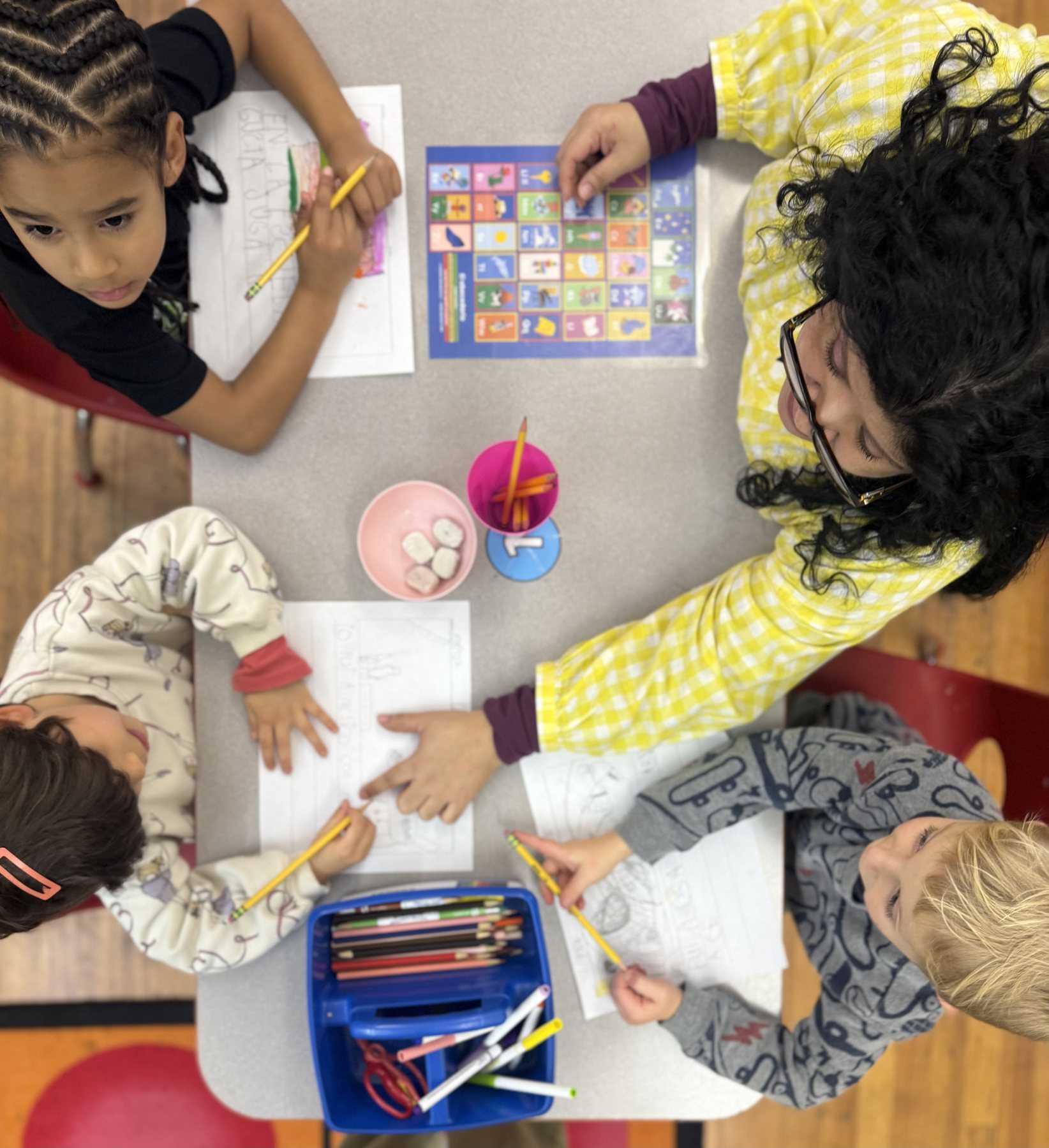 A teacher writing alongside four students at a classroom table