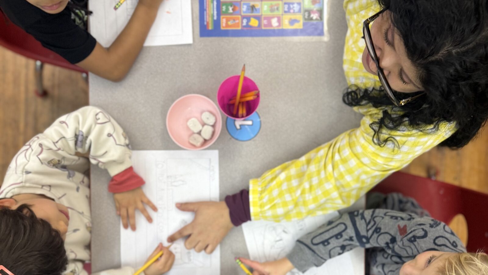 Students' hands sharing colored pencils around a classroom table