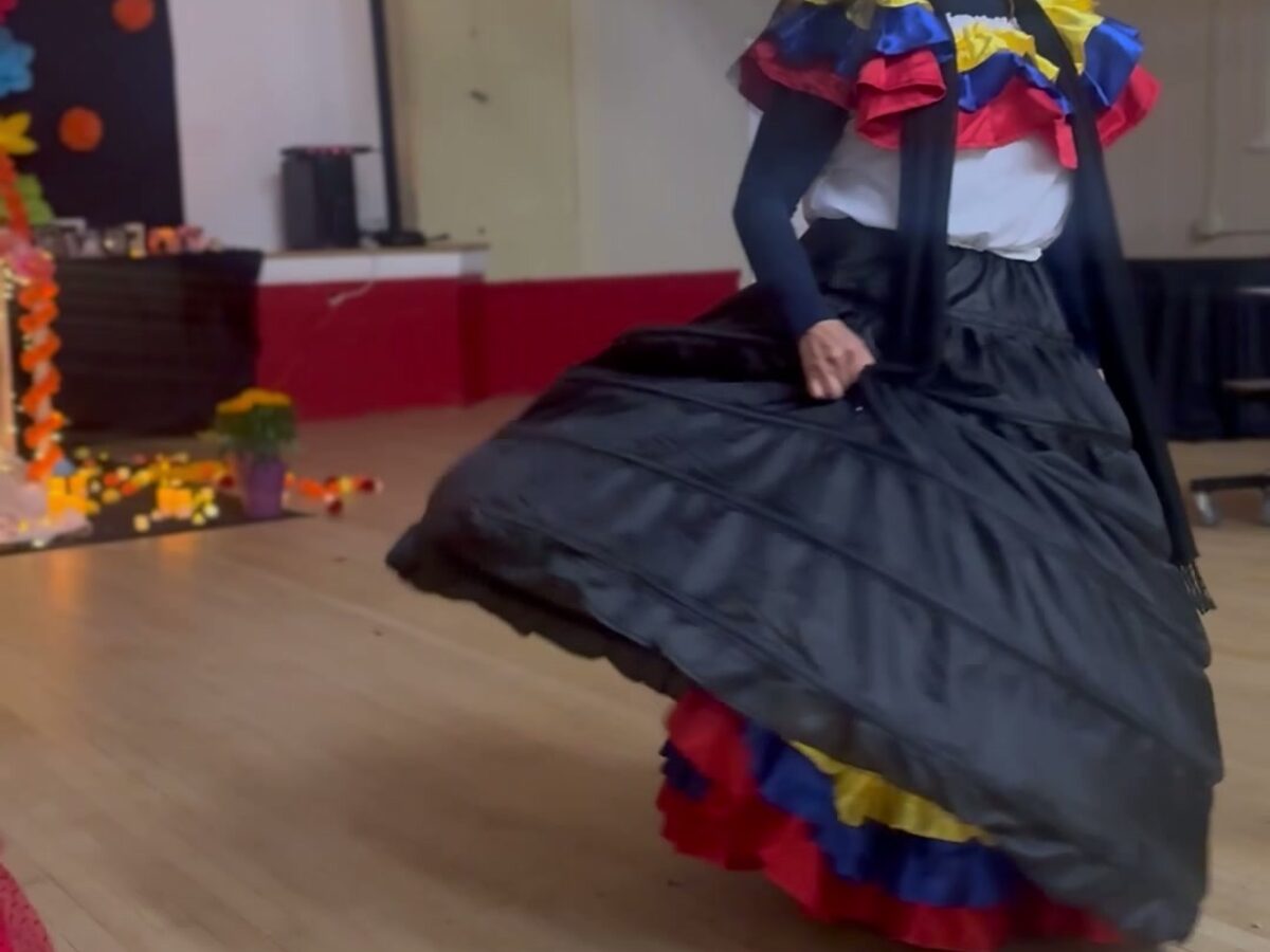 A dancer in a Día de Muertos dress performing for Amistad students in the gym